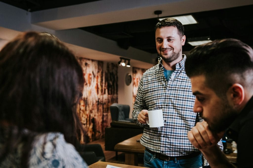 Three people chat and smile; one is holding a mug
